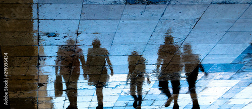 Reflection shadow silhouette on wet city sidewalk of mysterious people walking away the night