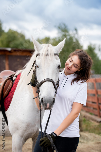 Young woman cuddling white racehorse and looking at her while chilling out