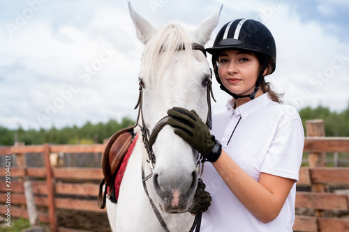 Calm woman in white polo shirt and equestrian outfit embracing purebred horse