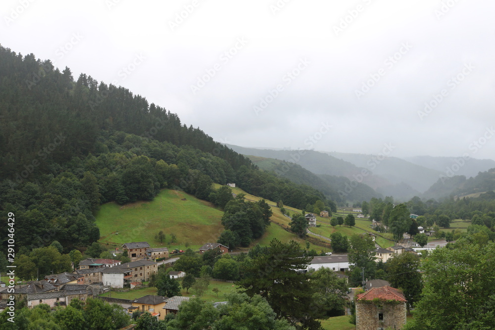 Fototapeta premium Village and mountains with gray sky, fog and rain