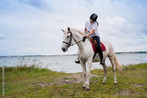 Active woman in equestrian outfit moving along river on back of white racehorse