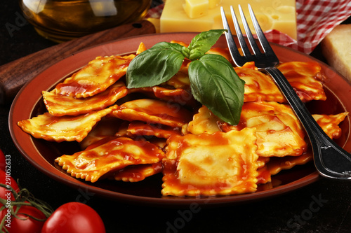 Ravioli with tomato sauce garnished with parmesan cheese and basil on rustic table