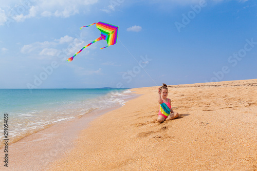 Child playing with a kite while running along the beach, in a summer sunny day. Have fun with your family during the holidays. Happy little girl launches a kite, summer vacation 