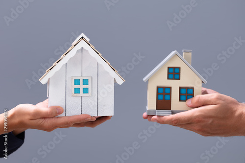 Fotografie Close-up Of Couple's Hand Holding Different Miniature Houses