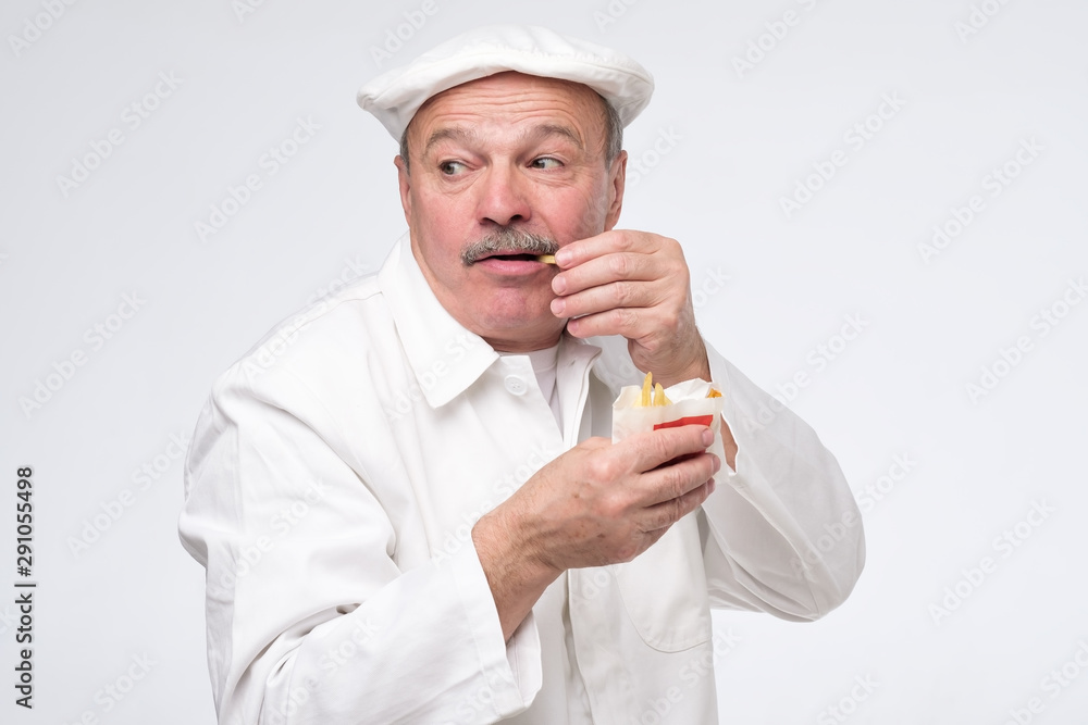 Funny hungry bearded male cook chef eating junk food isolated on white background looking aroung cautious. Studio shot Funny hungry bearded male cook chef eating junk food isolated on white background looking aroung cautious. Studio shot