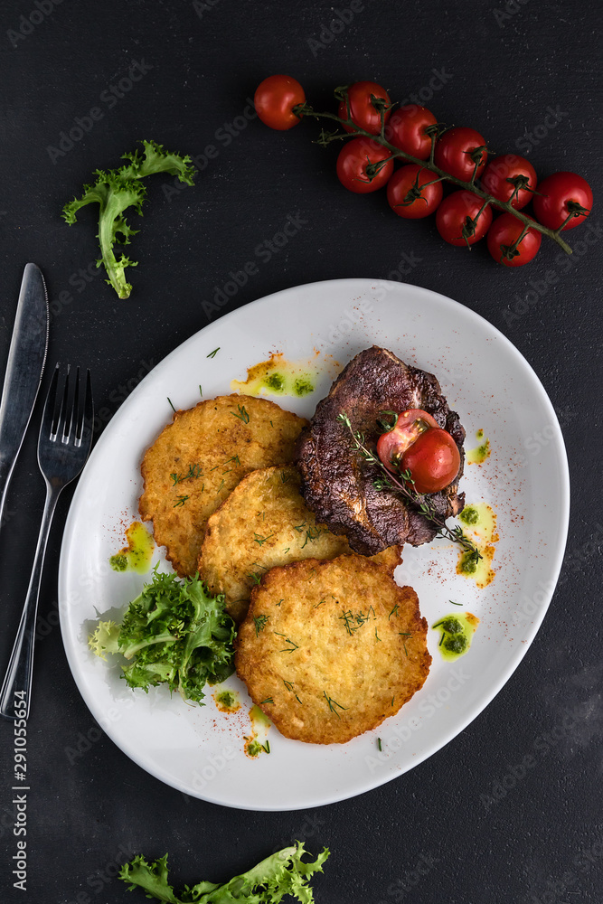 Top view Pork steak with pancakes with herbs and cherry tomatoes on a dark gray cement background Top view Pork steak with pancakes with herbs and cherry tomatoes on a dark gray cement background