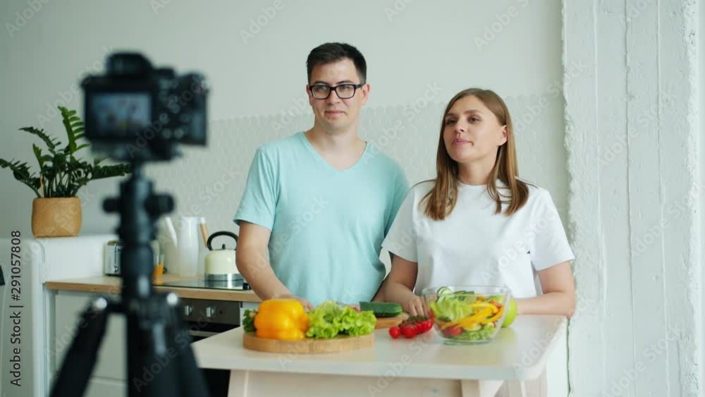 Man and woman couple are recording video for internet vlog in kitchen showing vegetables using camera talking and gesturing. Lifestyle and vlogging concept. Man and woman couple are recording video for internet vlog in kitchen showing vegetables using camera talking and gesturing. Lifestyle and vlogging concept.