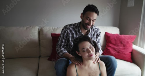Smiling boyfriend massaging girlfriend's neck while sitting on sofa at