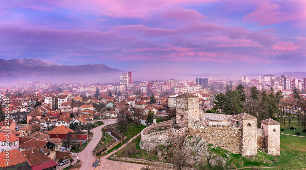 Colorful, magenta, sunset sky over misty cityscape panorama and foreground ancient fortress in Pirot, Serbia