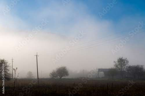 A moody, dull, morning with a fog with an farm house and power lines wires