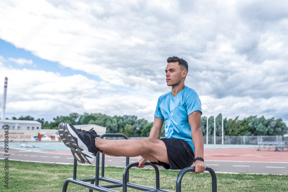 Male athlete summer training in city, grass clouds background, sports stadium, exercise on abdominal muscles, pump press, trainer strength motivation youth lifestyle, workout in nature.
