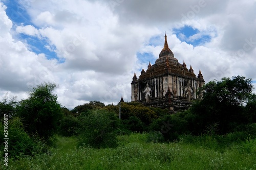 Thatbyinnyu Temple under sunny clouds blue sky. The highest pagoda in Bagan Myanmar. Forest and grass foreground 