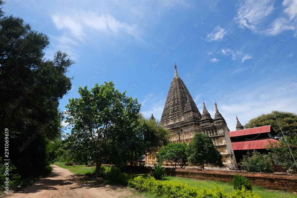 Wide angle view of Mahabodhi Temple in Bagan Myanmar under sunny blue sky. Pyramidal ancient buddhist pagoda. Green trees around