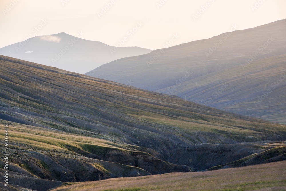 Icelandic landscape with a row of sloping mountains, the farthest partially hidden by haze, in the late afternoon light