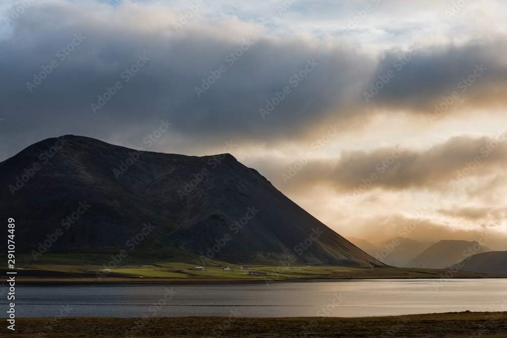 Icelandic landscape at sunset, with a lake in foreground and mountain in the background, under a cloudy sky