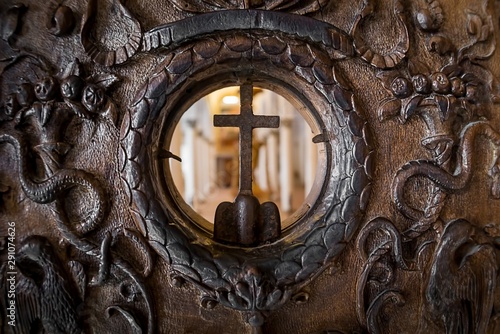 Close up of an ancient historiated wooden door, with a circular opening showing the room behind photo