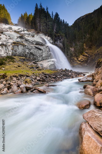 Low angle shot with rocks and a stream in foreground  and a waterfall in the background  in the Krimml park