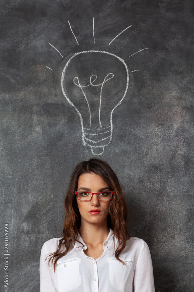 serious business woman in glasses near blackboard with lamp icon, idea symbol