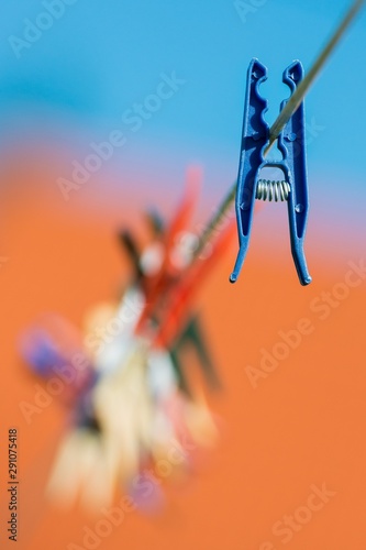 A blue clothes peg hanging far from the others, against a blue and orange bokeh background