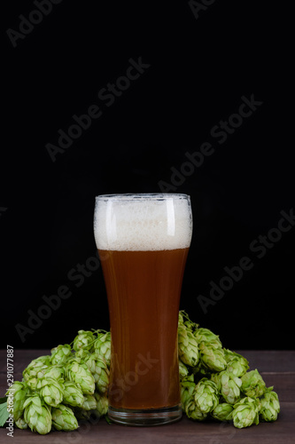 Beer with fresh green hops on black wooden table. Empty space for text. Black background