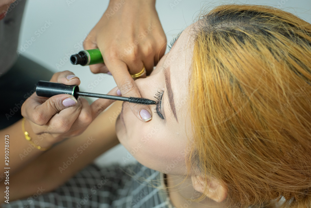 Makeup artist asian woman applying cosmetic mascara on eyelashes using curling brush. Makeup artist asian woman applying cosmetic mascara on eyelashes using curling brush.