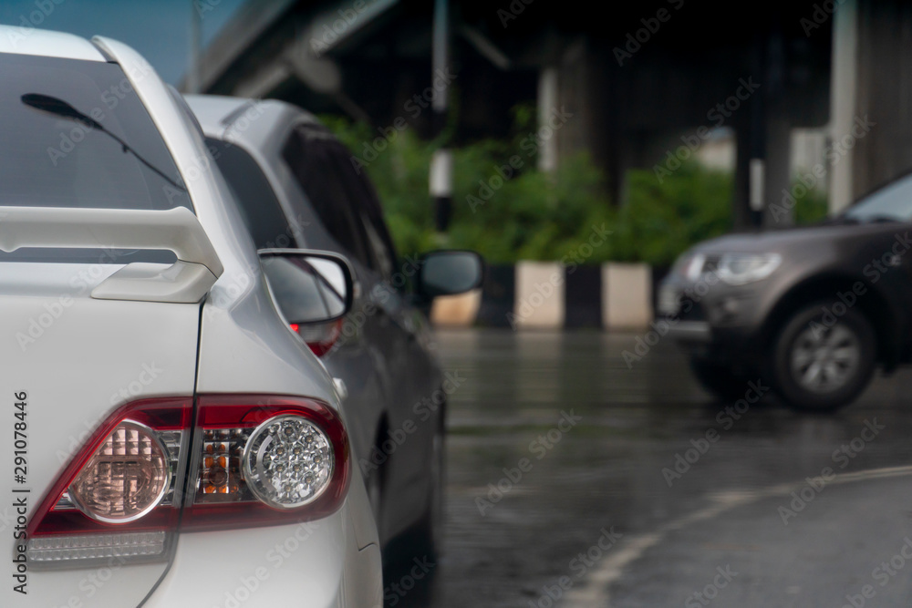 White car on asphalt roads during rainy time. Stop by traffic red light control. Park beside a different level bridge.