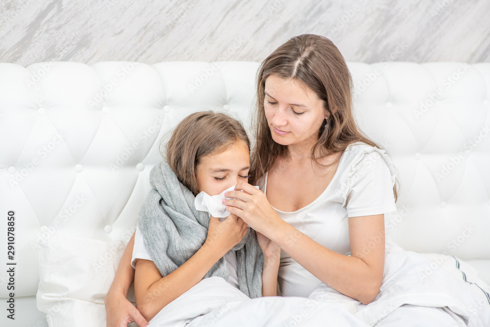 Young woman on the bed blowing the nose of her little girl Young woman on the bed blowing the nose of her little girl