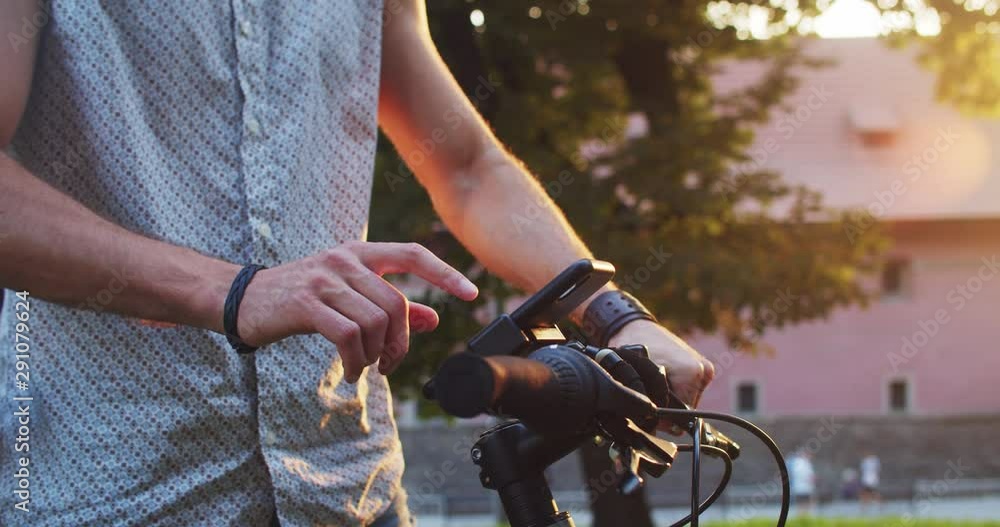 Young hipster riding a bicycle with attached smartphone on handlebar staying in lovely modern street at sunset. Young hipster riding a bicycle with attached smartphone on handlebar staying in lovely modern street at sunset.