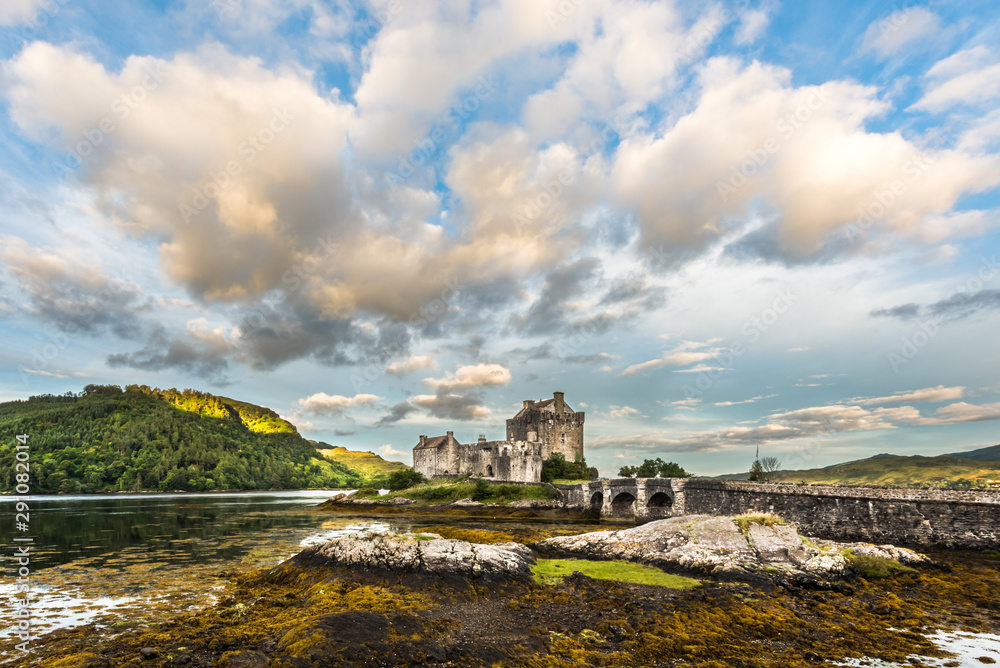 Ancient scottish castle sitting on a rock among seaweeds under a blue sky with puffy clouds in the early morning light