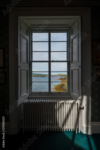 Interior of an old and elegant scottish house, with a window overlooking the coastline and distant islands 