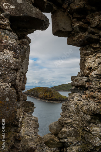 Through an opening on a rock wall can be seen the sea and a small island