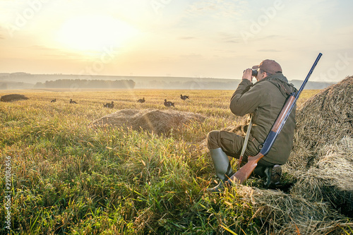 The man is on the hunt. Hunting period, autumn season. Male with a gun and binoculars at dawn. Hant on birg grouse. photo