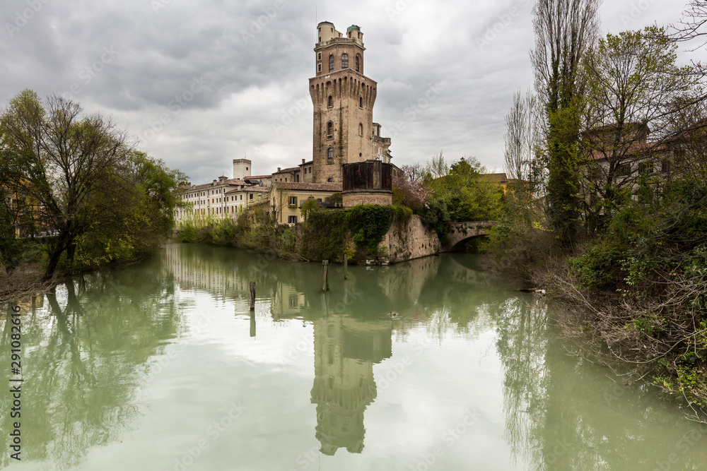 An italian medieval tower used as an astronomical observatory, reflecting on water under a cloudy sky