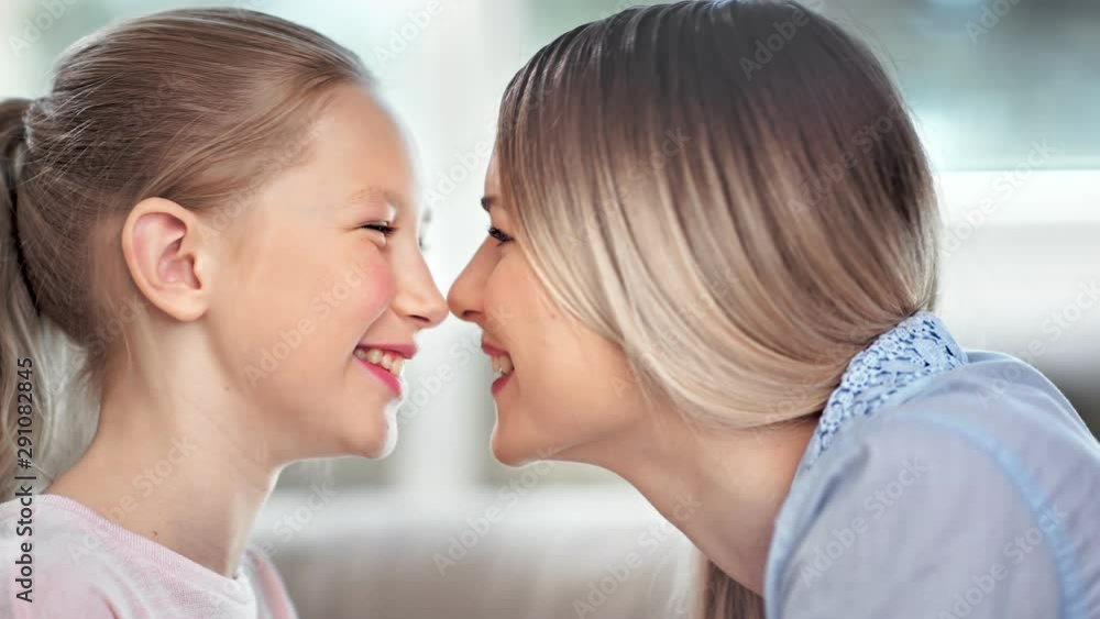 Pretty family young mother and child daughter smiling with open mouth showing teeth playing touching nose Pretty family young mother and child daughter smiling with open mouth showing teeth playing touching nose