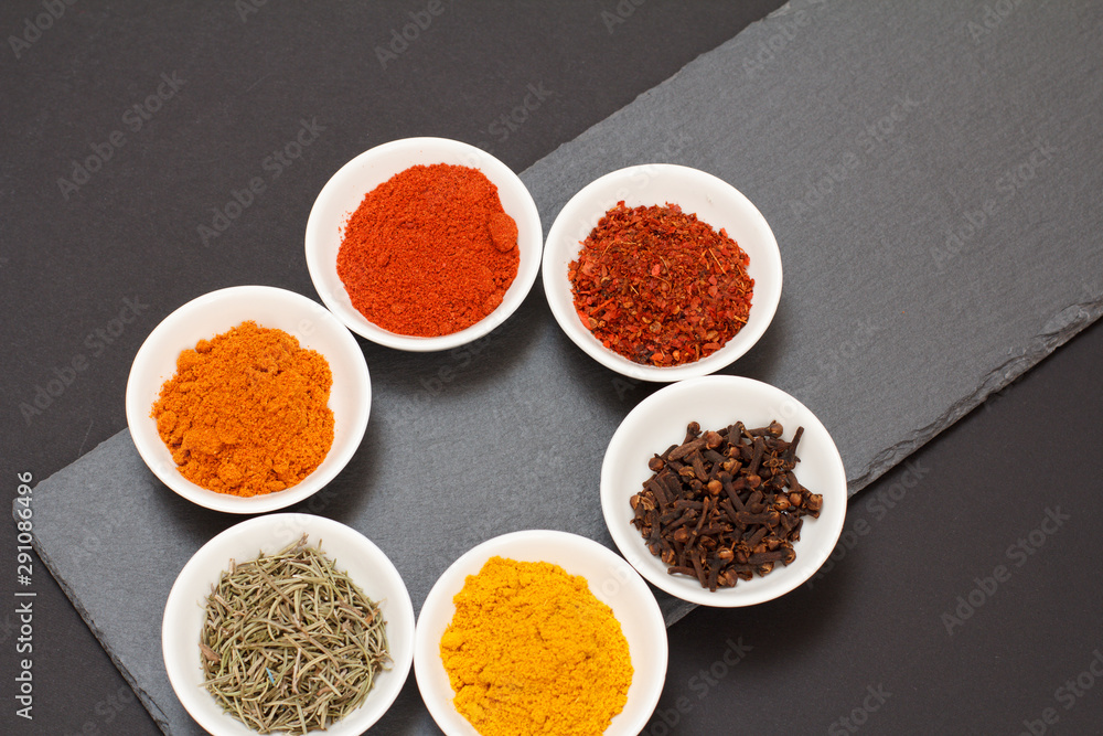 Various ground spices and herbs on stone cutting board.