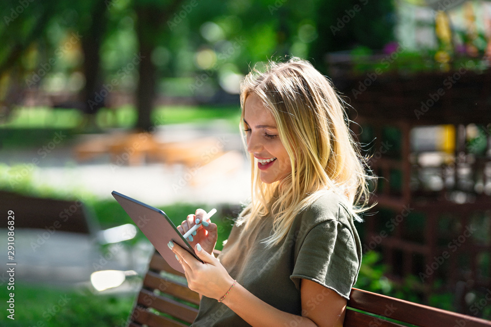 Young happy smiling woman with tablet on the bench - obrazy, fototapety, plakaty 