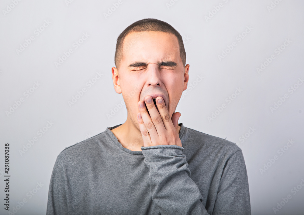 Tired wanting to sleep young man yawning and closed mouth the hand on blue background. Tired wanting to sleep young man yawning and closed mouth the hand on blue background.