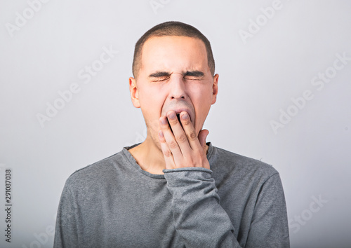 Tired wanting to sleep young man yawning and closed mouth the hand on blue background.