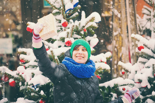 Woman with a Christmas present near a decorated city tree.