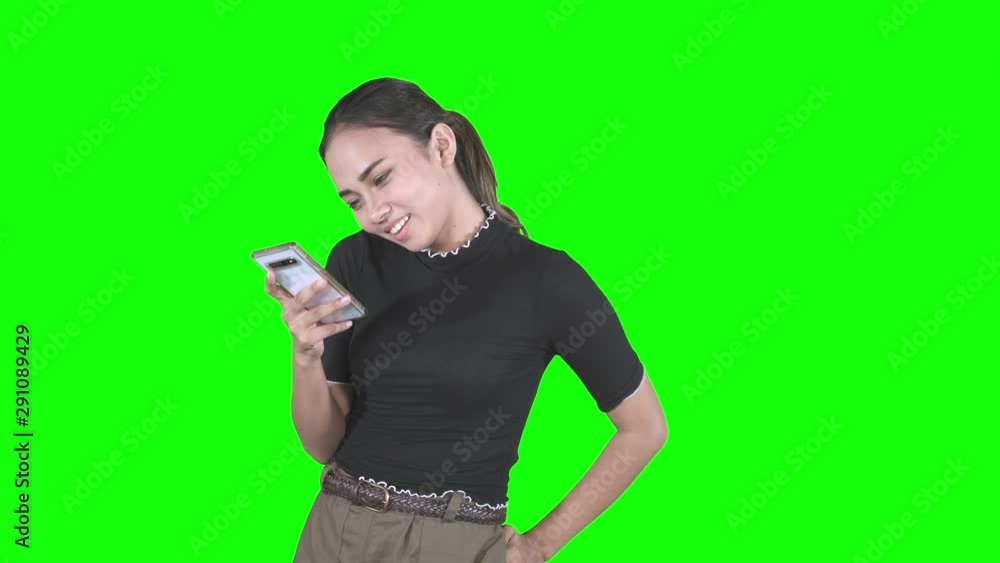 Happy teenager girl reading a message on the smartphone while smiling and standing in the studio. Shot in 4k resolution with green screen background Happy teenager girl reading a message on the smartphone while smiling and standing in the studio. Shot in 4k resolution with green screen background