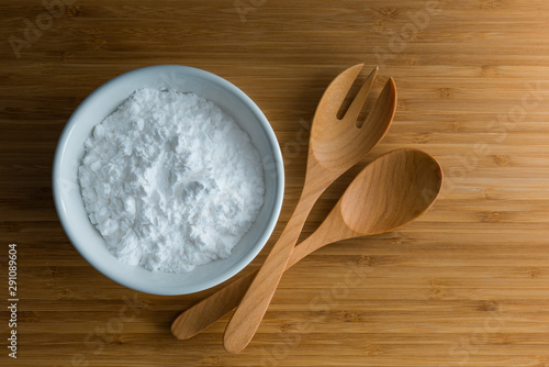 Top view tapioca starch/flour powder in white bowl with wooden background, spoon and fork