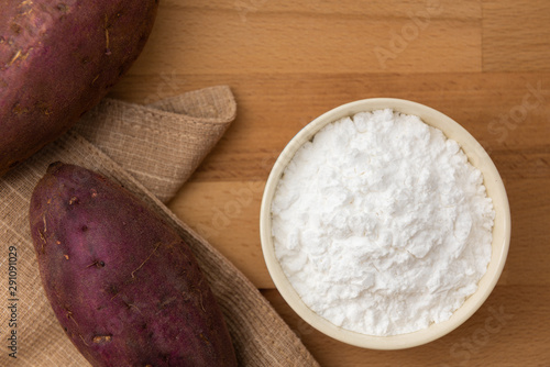 Top view of sweet potato starch in white bowl with sweet potato wooden table background