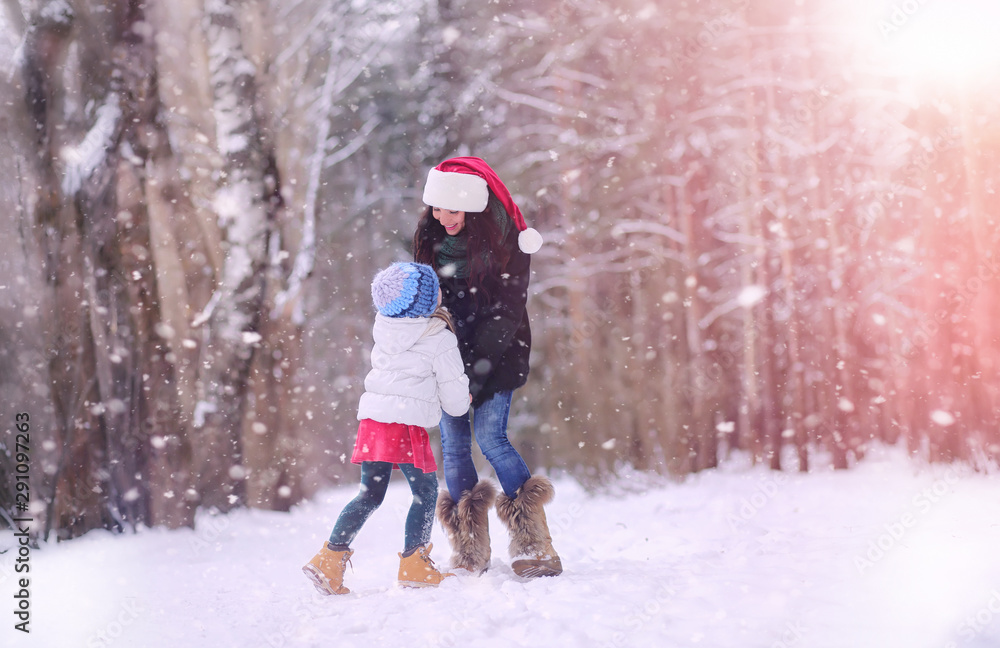 A winter fairy tale, a young mother and daughter  in the forest. A girl on a sled with gifts on the eve of the new year in the park. Two sisters walk in a New Year's park and ride a sled with gifts.