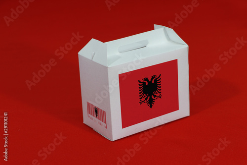Albanian flag on white box with barcode and the color of nation flag on red background. The concept of export trading from Albania.