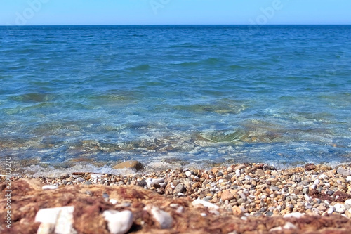 Natural seascape background. Sea stone pebble beach with clear blue water and small waves rolling to shore. Beautifull wild place.