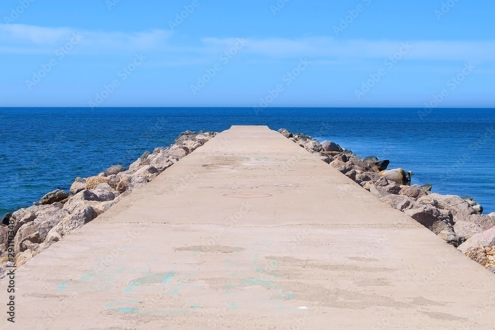 Seascape background with empty long stone concrete pier stretching out to sea at sunny day. Cement pier with rocks on edges. Clear blue sky and water. Seascape background with empty long stone concrete pier stretching out to sea at sunny day. Cement pier with rocks on edges. Clear blue sky and water.