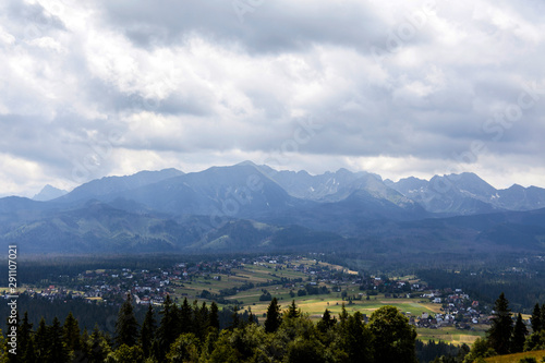 Tatra mountains wide angle panorama. Tatras high contrast wallpaper dramatic background. White clouds and dark forests. Full panorama of the whole mountain range, small villages below the hills