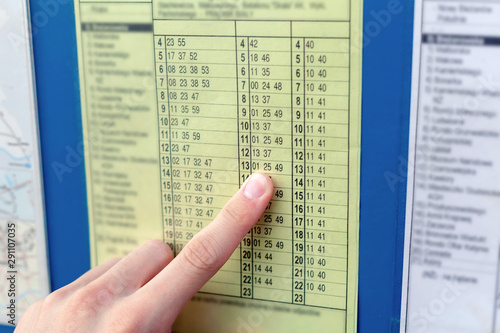Man checking a yellow bus timetable pointing his finger at the hour of bus arrival. Public transportation, travelling by train or a bus, arriving on time or late concept, punctuality