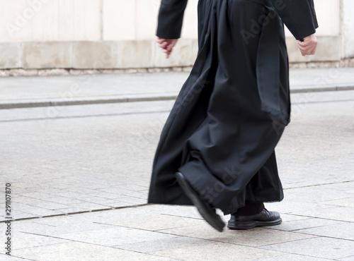 Fototapeta Catholic priest in the black cassock walking on the street solo, only legs visible