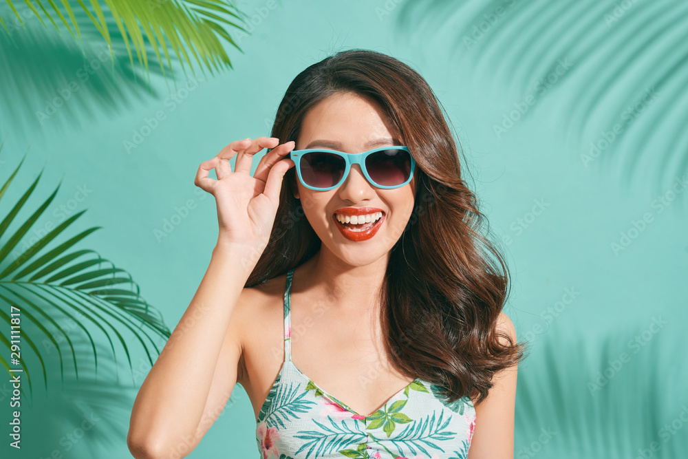 Asian young woman wearing a bikini and sunglasses having fun on blue background Asian young woman wearing a bikini and sunglasses having fun on blue background